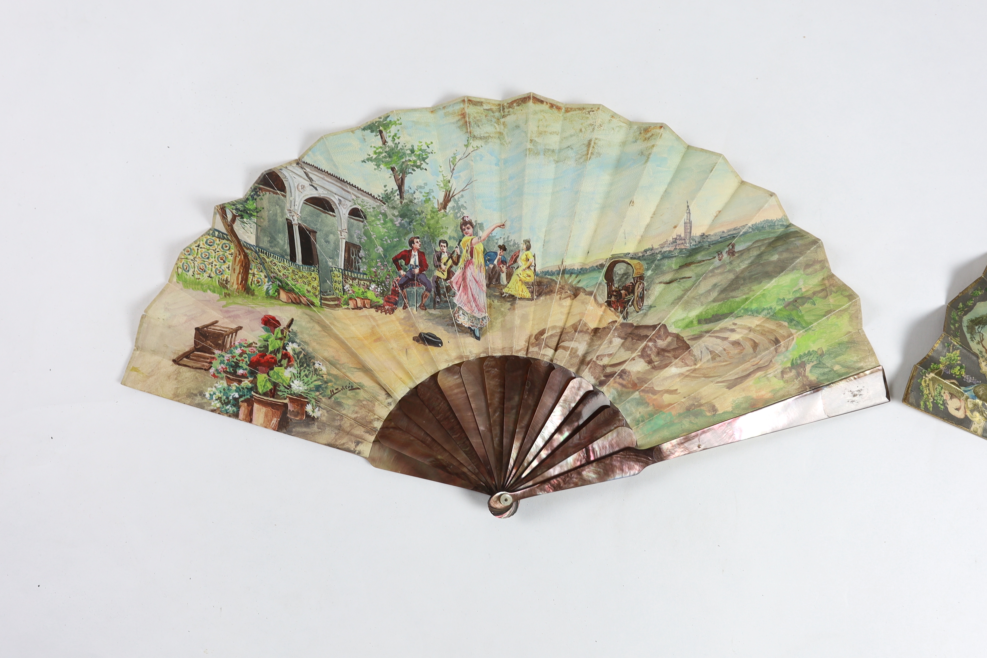 A 19th century mother of pearl and carved bone fan with ornate printed paper leaf, together with a similar Spanish fan of dancers, with mother of pearl guards, signed.